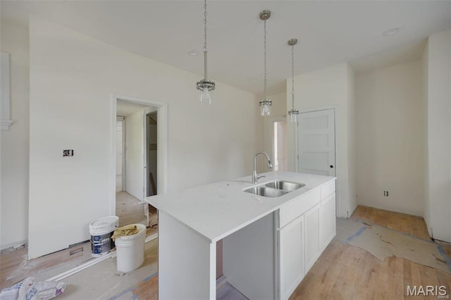 kitchen with a sink, hanging light fixtures, white cabinets, a center island with sink, and light countertops