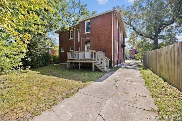 rear view of house featuring a wooden deck, brick siding, driveway, and stairs