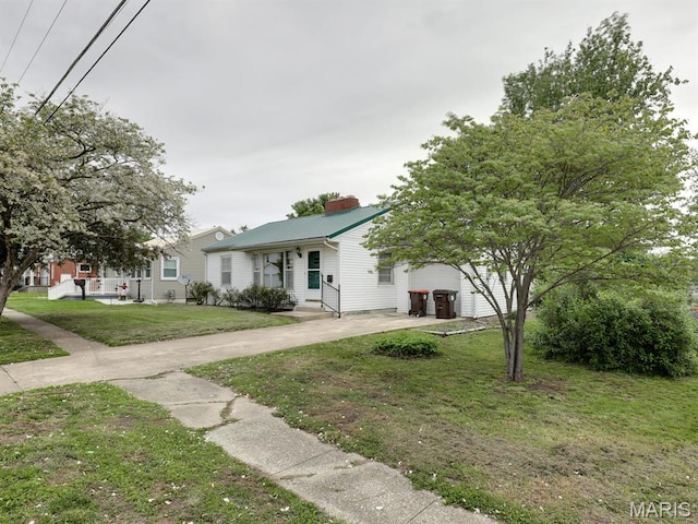 view of front of house featuring driveway, a chimney, a front yard, metal roof, and a garage