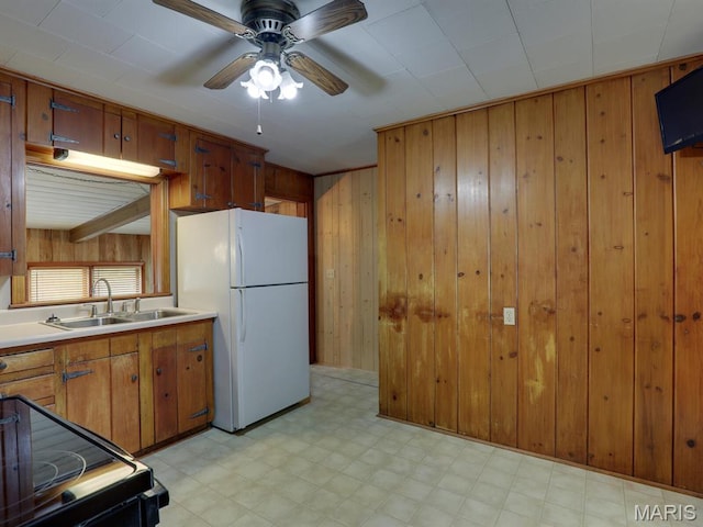 kitchen with freestanding refrigerator, wooden walls, a sink, light flooring, and a ceiling fan