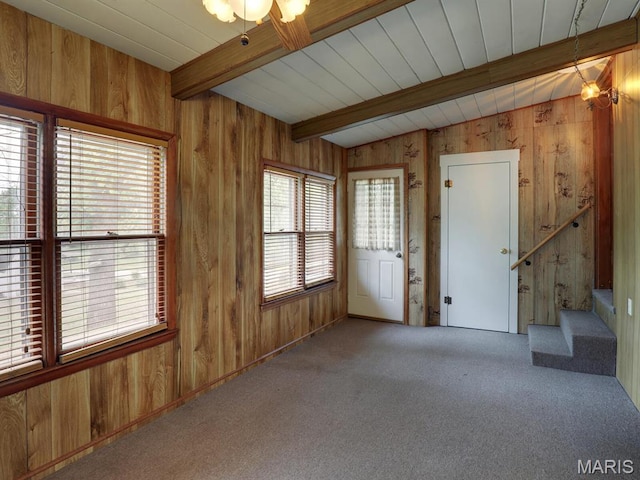 carpeted empty room with wood walls, beam ceiling, and stairs