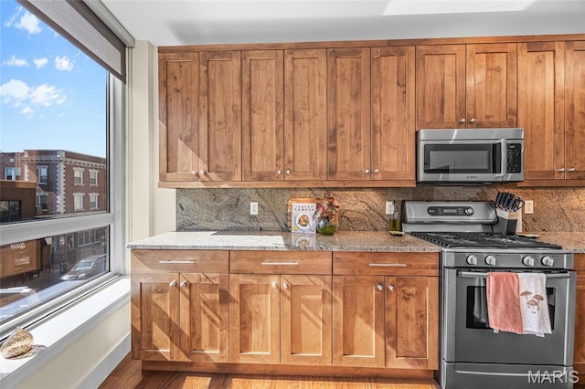 9 N Euclid Ave Unit 303, Saint Louis, MO 63108 - kitchen featuring appliances with stainless steel finishes, tasteful backsplash, brown cabinets, light stone counters, and light wood finished floors