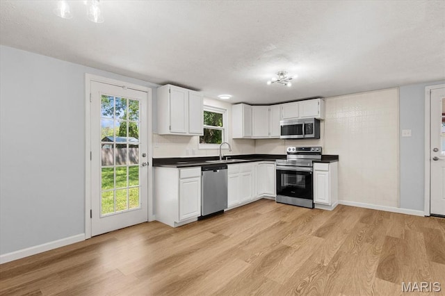 kitchen with stainless steel appliances, a sink, light wood finished floors, and baseboards