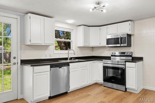 kitchen featuring stainless steel appliances, a sink, dark countertops, plenty of natural light, and a textured ceiling