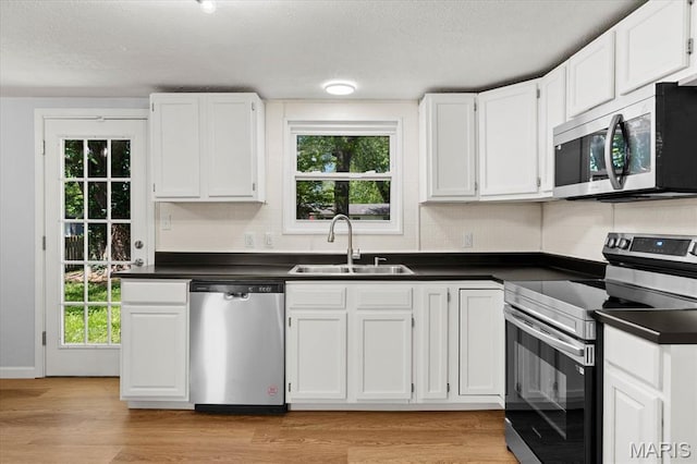 kitchen featuring stainless steel appliances, a sink, dark countertops, a textured ceiling, and white cabinetry