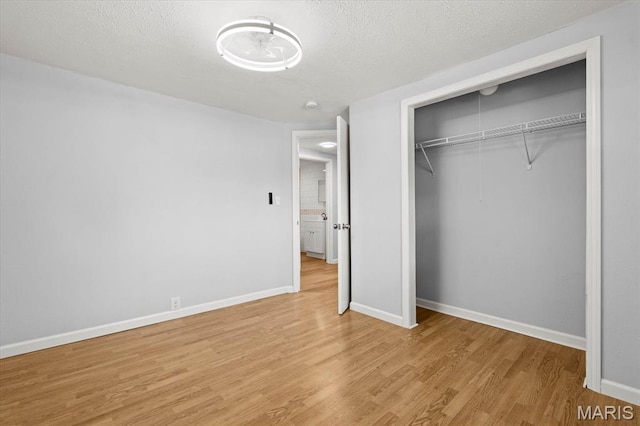unfurnished bedroom featuring light wood-style floors, baseboards, a closet, and a textured ceiling