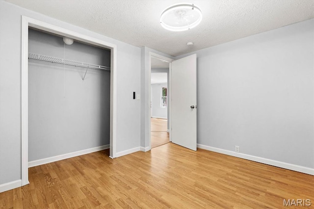 unfurnished bedroom with light wood-style floors, a textured ceiling, baseboards, and a closet