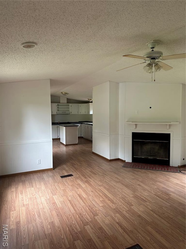 2557 River Bend Rd, Saint Clair, MO 63077 - unfurnished living room with dark wood finished floors, a textured ceiling, ceiling fan, a wainscoted wall, and a glass covered fireplace
