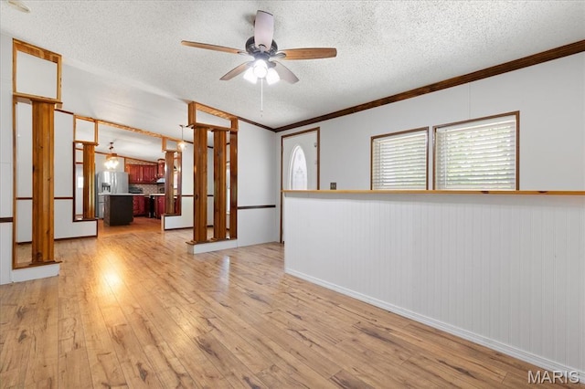 unfurnished living room featuring a ceiling fan, a textured ceiling, light wood-style floors, ornamental molding, and wainscoting