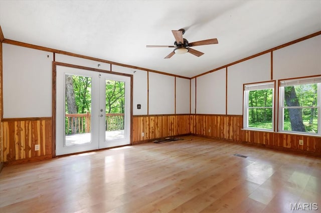 unfurnished room with french doors, lofted ceiling, a ceiling fan, light wood-type flooring, and a wainscoted wall