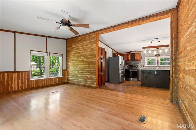 unfurnished living room featuring wood walls, light wood finished floors, and ceiling fan