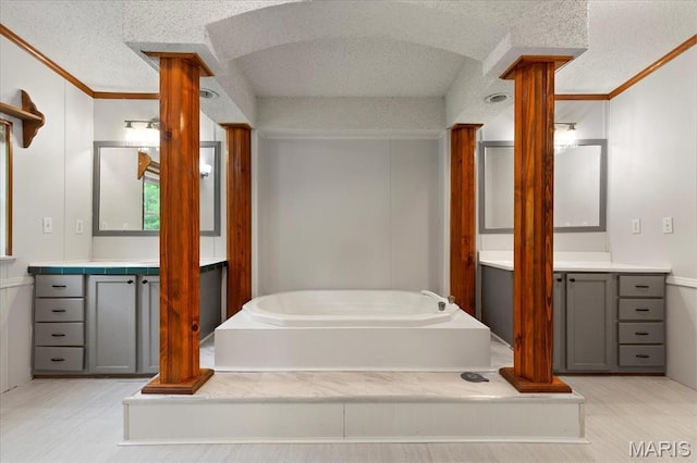 full bath featuring a textured ceiling, crown molding, a garden tub, vanity, and decorative columns