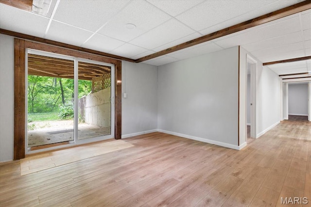 spare room with light wood-type flooring, a paneled ceiling, and baseboards