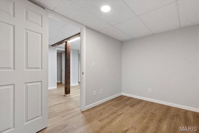 empty room with light wood-type flooring, a drop ceiling, and baseboards