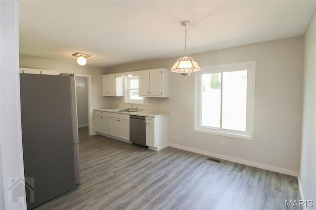 104 Wild Rose Pl, Saint Robert, MO 65584 - kitchen with stainless steel appliances, light countertops, light wood-style floors, white cabinetry, and decorative light fixtures