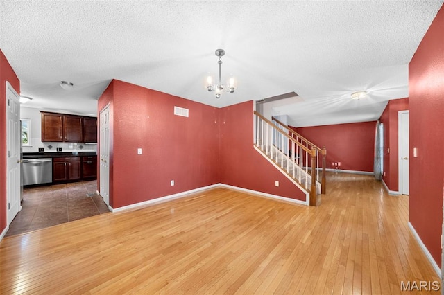 14 Sunderland Ct, Saint Charles, MO 63303 - unfurnished living room with light wood finished floors, stairs, a chandelier, baseboards, and a textured ceiling