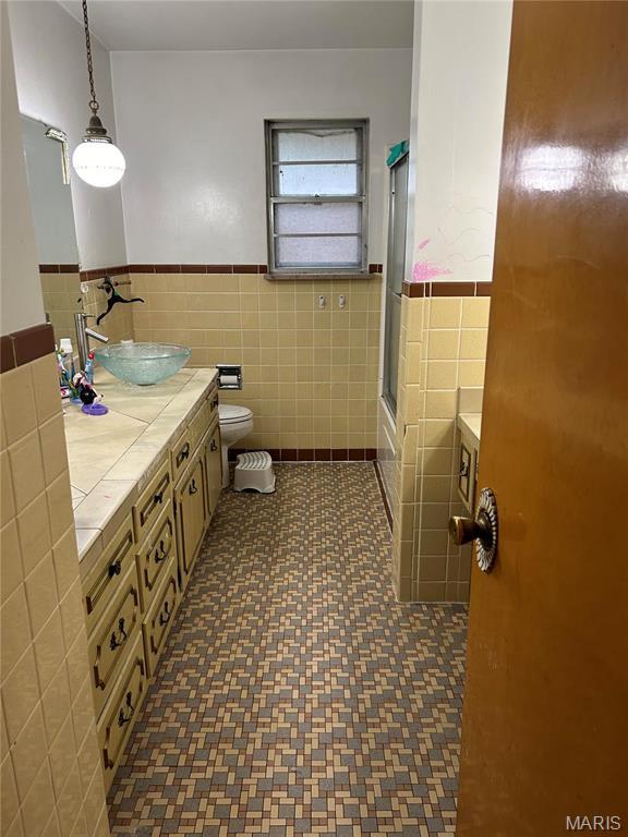 full bath featuring tile walls, wainscoting, toilet, vanity, and enclosed tub / shower combo
