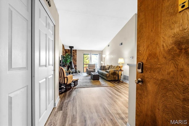 entrance foyer with wood finished floors, lofted ceiling, baseboards, and a wood stove