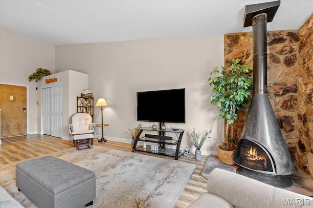 living area featuring a wood stove, wood finished floors, baseboards, and vaulted ceiling