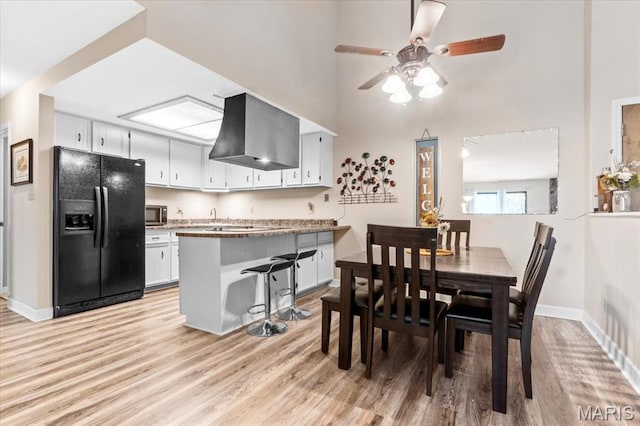 dining space with light wood-style flooring, baseboards, a ceiling fan, and a towering ceiling