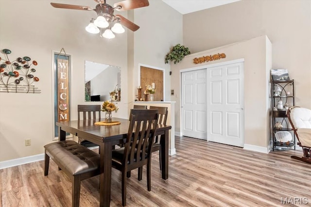 dining area with ceiling fan, light wood-style flooring, baseboards, and a high ceiling