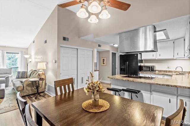 dining space featuring a ceiling fan, light wood-type flooring, baseboards, and high vaulted ceiling