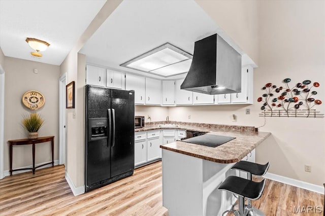 kitchen with black appliances, island range hood, a peninsula, a sink, and light wood-style floors