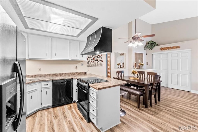 kitchen with black appliances, wall chimney exhaust hood, a peninsula, a ceiling fan, and light countertops