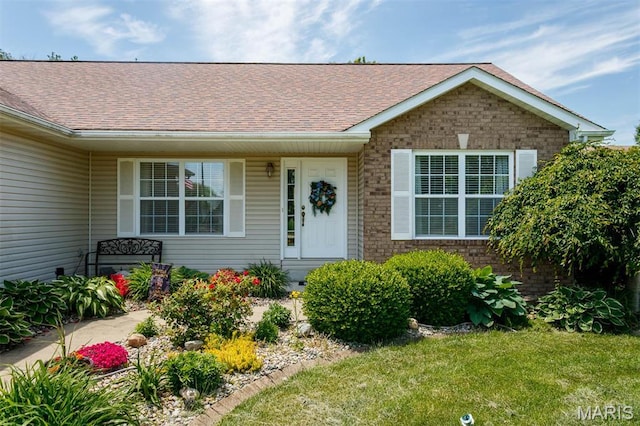entrance to property with roof with shingles, brick siding, and a yard