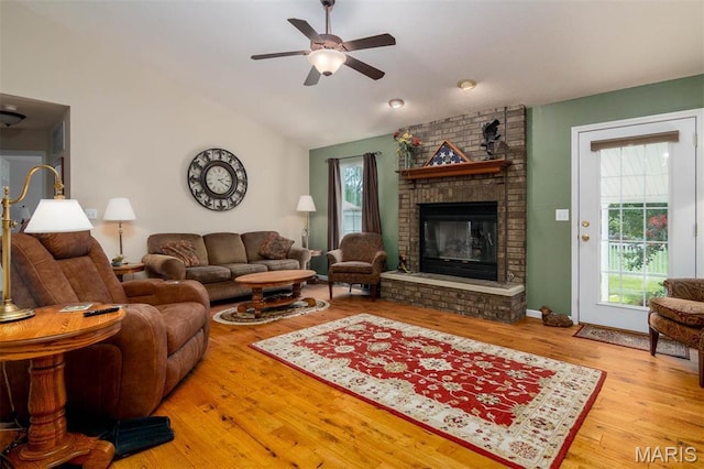living area with a ceiling fan, a brick fireplace, vaulted ceiling, and wood finished floors