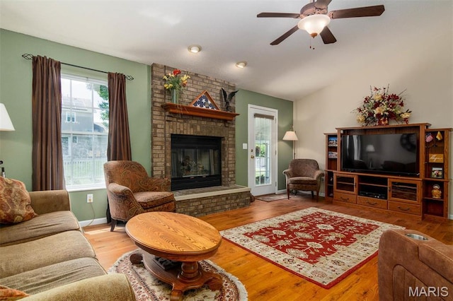 living area with a fireplace, wood finished floors, ceiling fan, vaulted ceiling, and baseboards