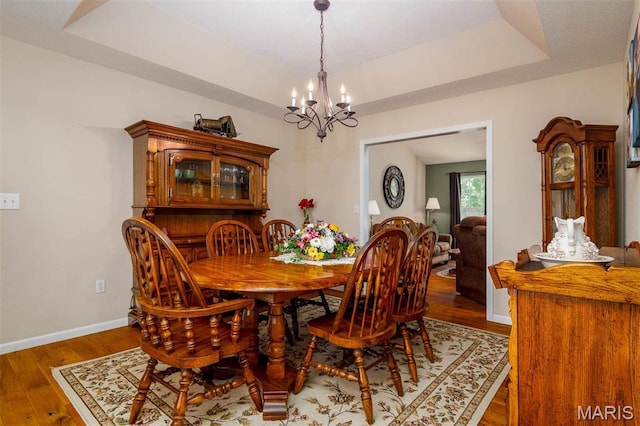 dining room featuring a chandelier, baseboards, wood finished floors, and a raised ceiling