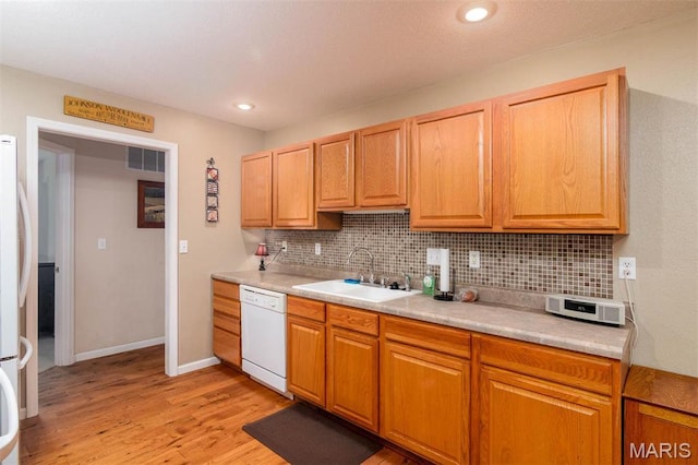 kitchen featuring white dishwasher, a sink, backsplash, light countertops, and light wood finished floors