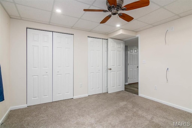 unfurnished bedroom featuring multiple closets, carpet flooring, baseboards, a drop ceiling, and recessed lighting