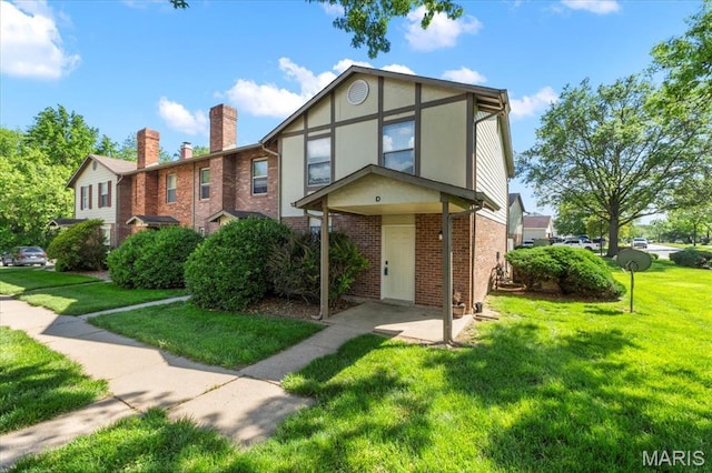 view of front of house featuring brick siding, a front lawn, a chimney, and stucco siding