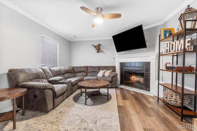 living room featuring wood finished floors, crown molding, a tiled fireplace, and a ceiling fan