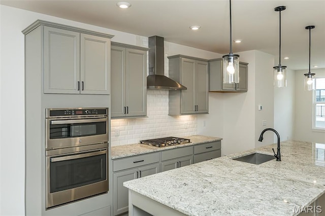 kitchen with gray cabinetry, wall chimney exhaust hood, appliances with stainless steel finishes, a sink, and recessed lighting
