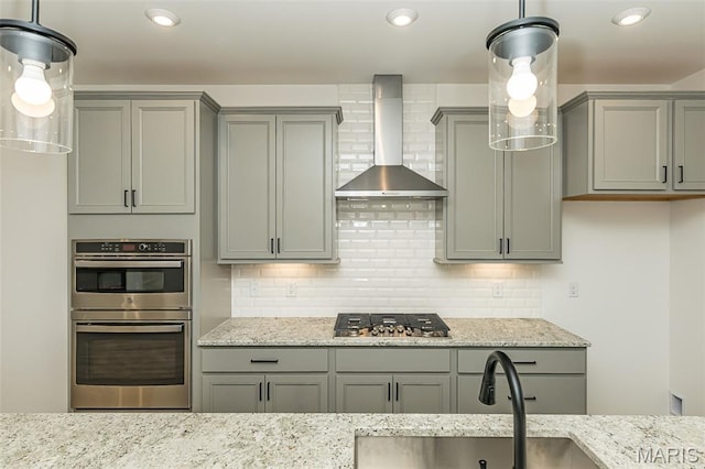 kitchen with gray cabinetry, wall chimney range hood, stainless steel appliances, a sink, and light stone countertops
