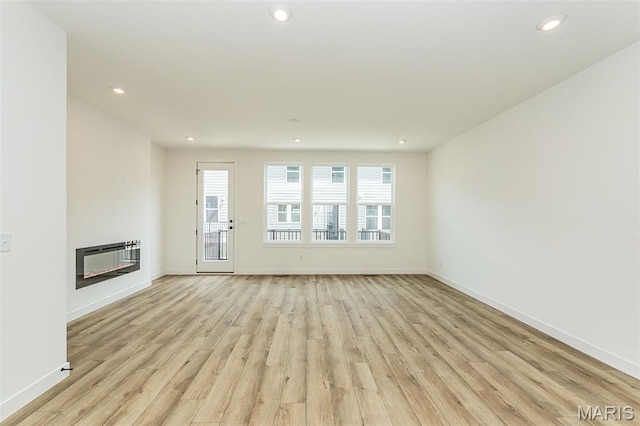 unfurnished living room with a glass covered fireplace, light wood-style floors, recessed lighting, and baseboards