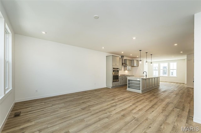 unfurnished living room with light wood finished floors, baseboards, a sink, and recessed lighting