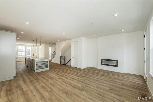 unfurnished living room with a sink, wood finished floors, baseboards, recessed lighting, and a glass covered fireplace