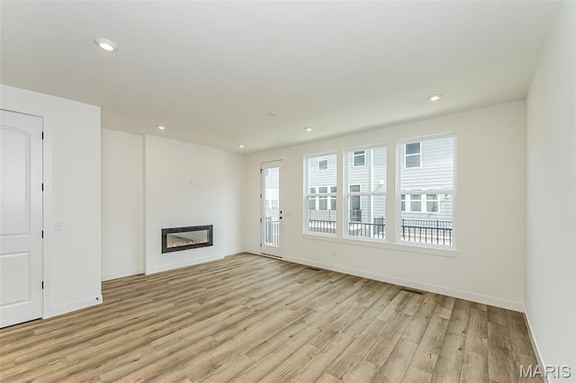 unfurnished living room with light wood-style flooring, baseboards, a glass covered fireplace, and recessed lighting
