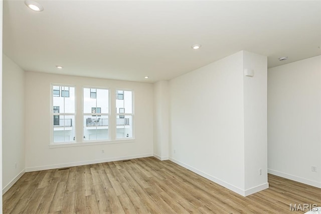 empty room featuring light wood finished floors, baseboards, recessed lighting, and a smoke detector