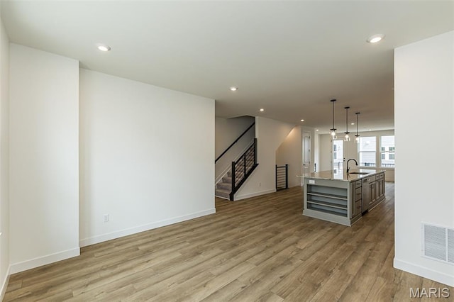 unfurnished living room with light wood-style floors, baseboards, stairway, recessed lighting, and a sink