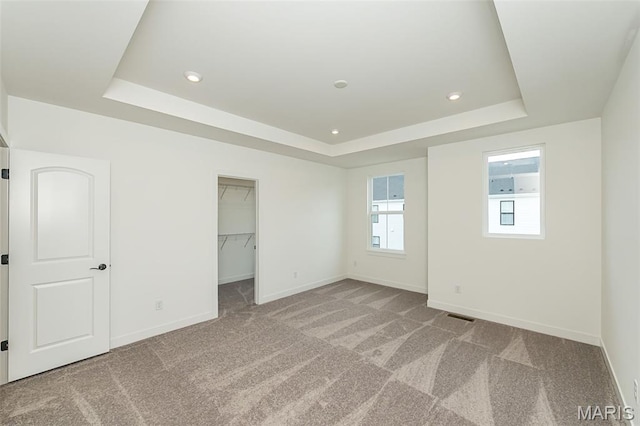unfurnished bedroom with a tray ceiling, carpet, baseboards, a walk in closet, and recessed lighting