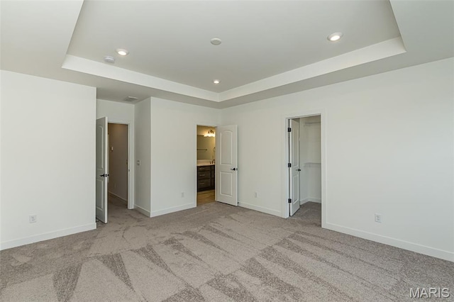 unfurnished bedroom with a tray ceiling, baseboards, light carpet, recessed lighting, and a walk in closet