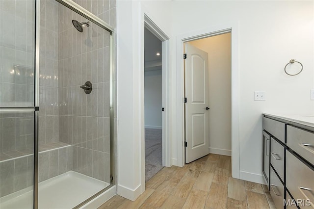 bathroom featuring a stall shower, wood finished floors, baseboards, and vanity