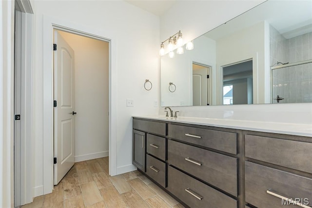 bathroom with a stall shower, vanity, wood finished floors, and baseboards