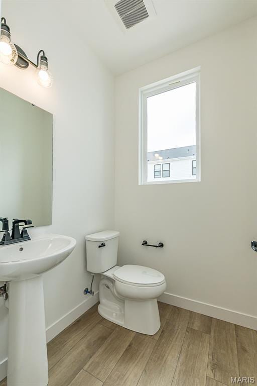 half bath featuring toilet, wood finished floors, baseboards, and a sink