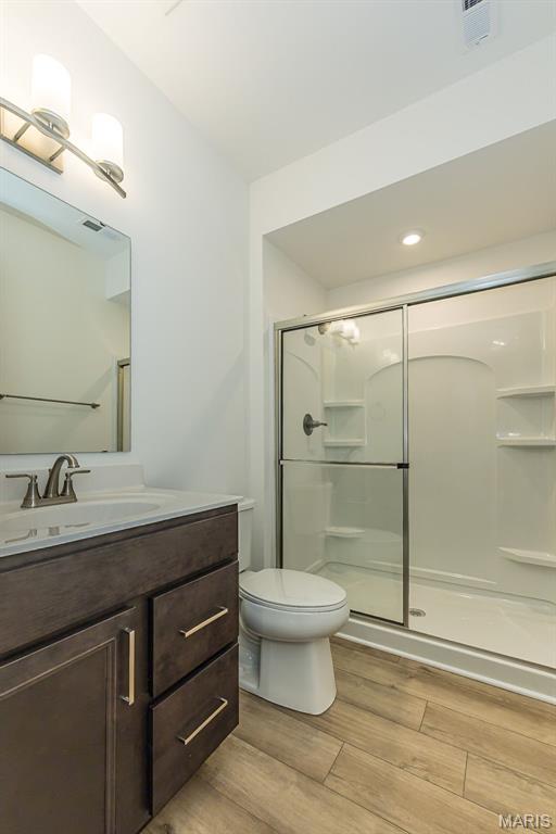 bathroom with wood finished floors, a stall shower, toilet, and vanity